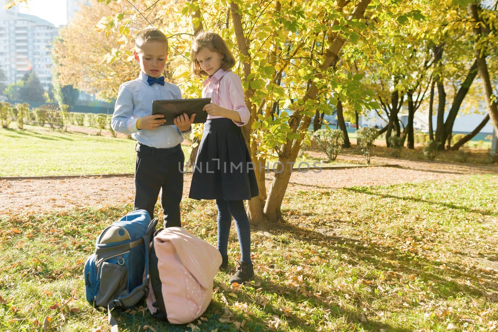 Two kids watching digital tablet, background autumn sunny park by VH-studio