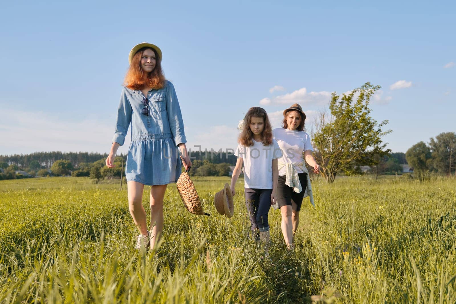 Mother with children two daughters walking along a country road, background summer meadow sunset