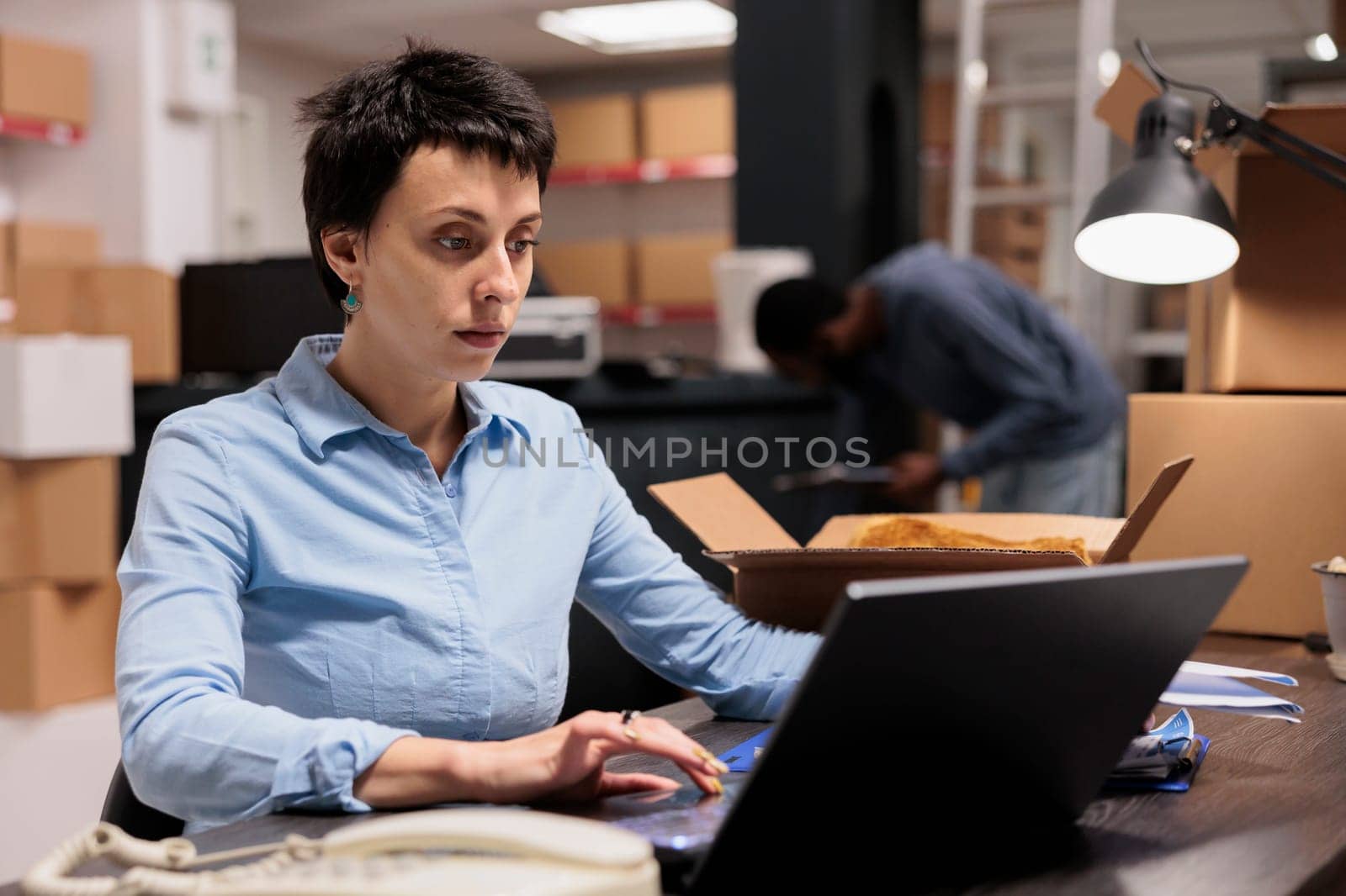 Storehouse manager sitting at desk table looking at online orders before start preparing customers packages, checking cargo stock. Supervisor woman working in warehouse delivery department