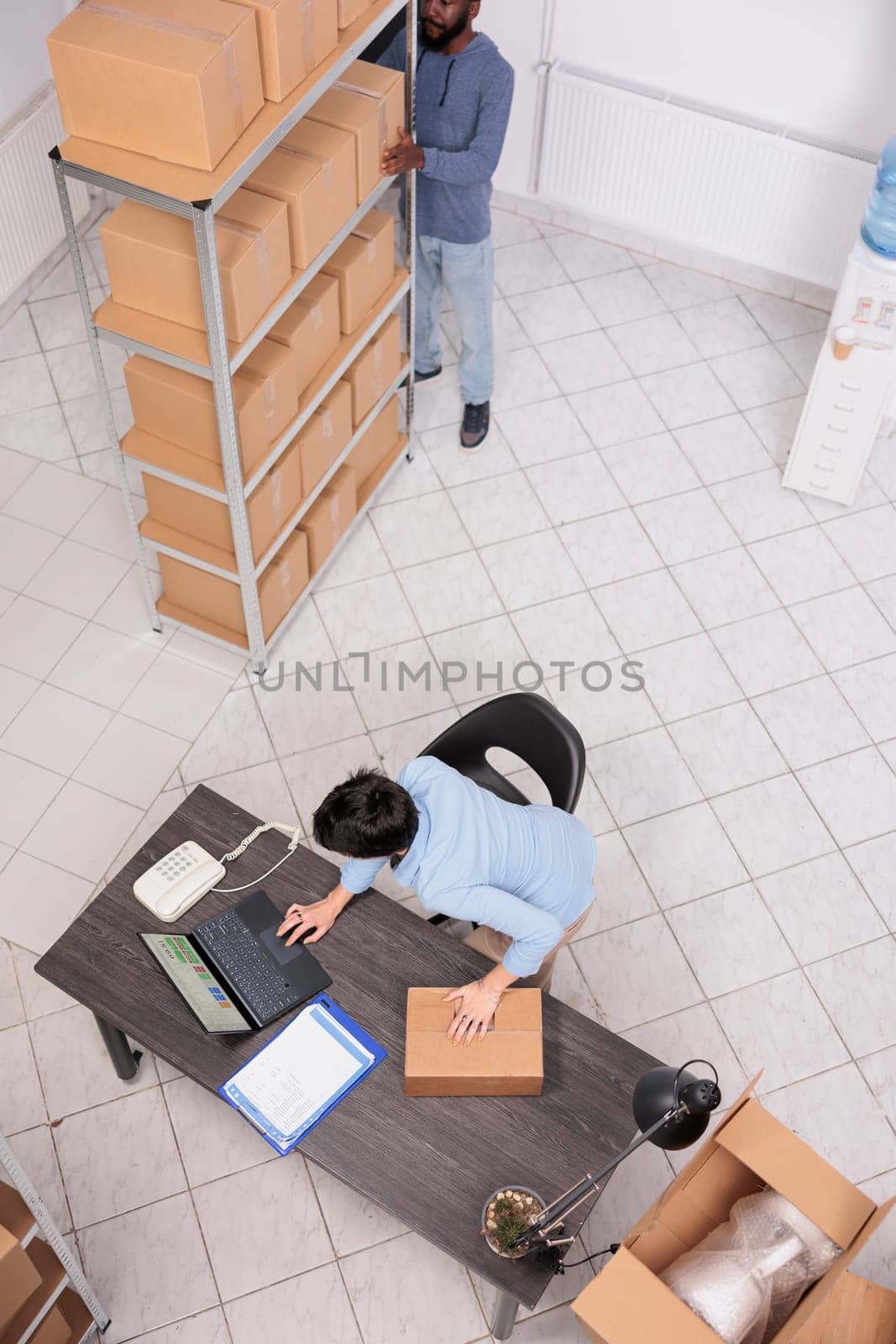 Top view of storehouse manager standing at desk in warehouse while preparing customer order by DCStudio