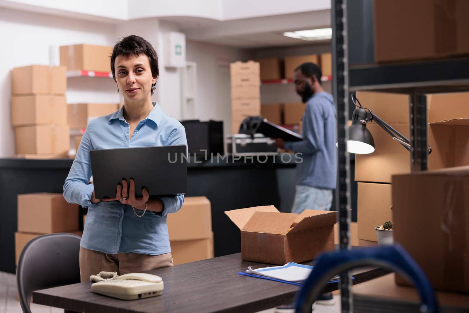 Storehouse manager holding laptop computer checking shipping detalies while working at clients orders, putting packages in carton box preparing for delivery. Distribution center fulfillment company