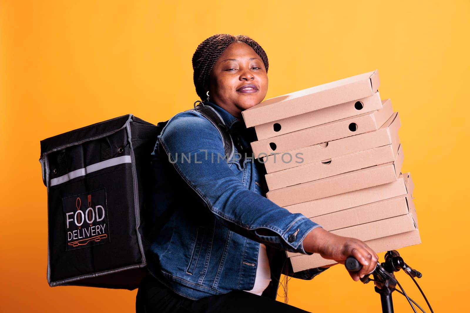 Pizzeria delivery worker carrying stack of cardboard full with pizza delivering takeaway food order to customer during lunch time, standing in studio. Restaurant employee using bike as transportation