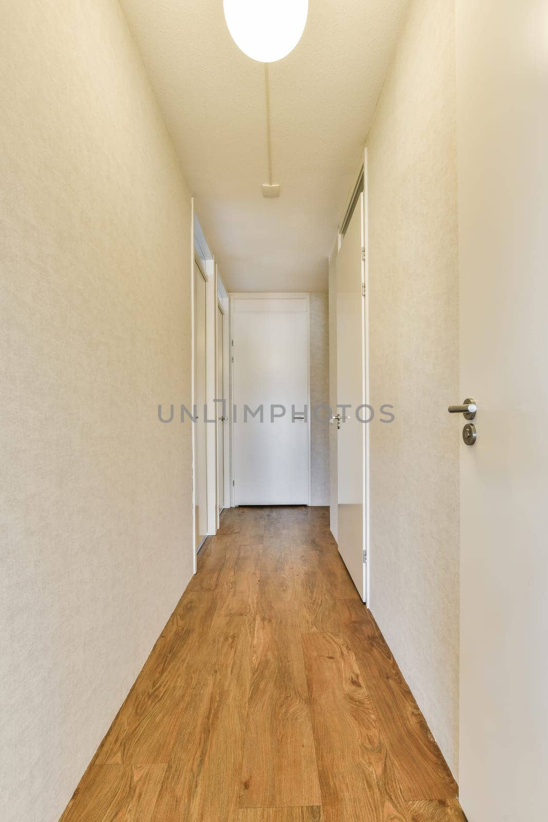 a long hallway with wood flooring and white walls on either side of the room, there is an open door