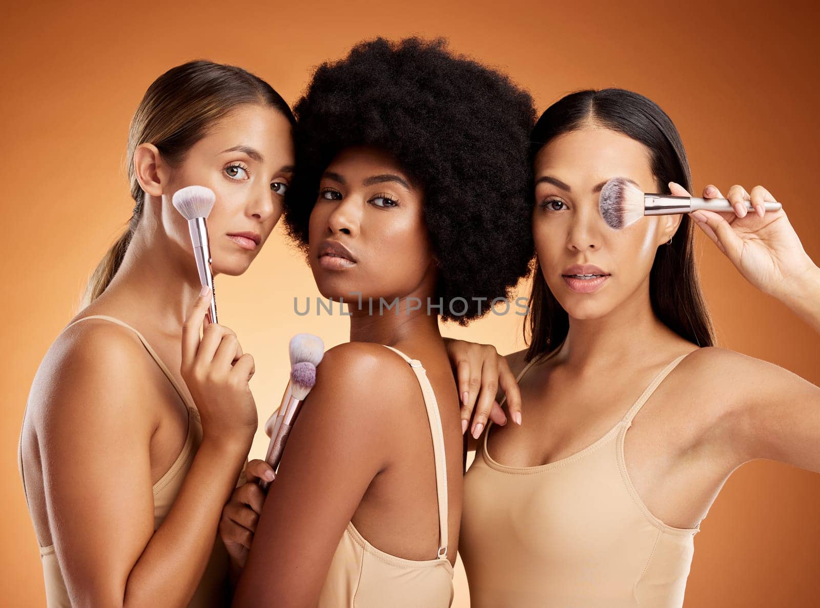 Makeup, beauty and women with brush for cosmetics against a brown mockup studio background. Portrait of young model group with cosmetic facial foundation and a luxury product for skin wellness by YuriArcurs