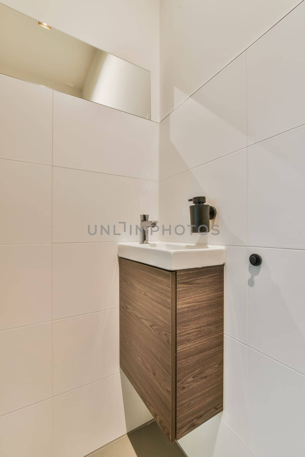 a bathroom with white tiles on the wall and wooden cabinet in the corner to the toilet is next to the sink