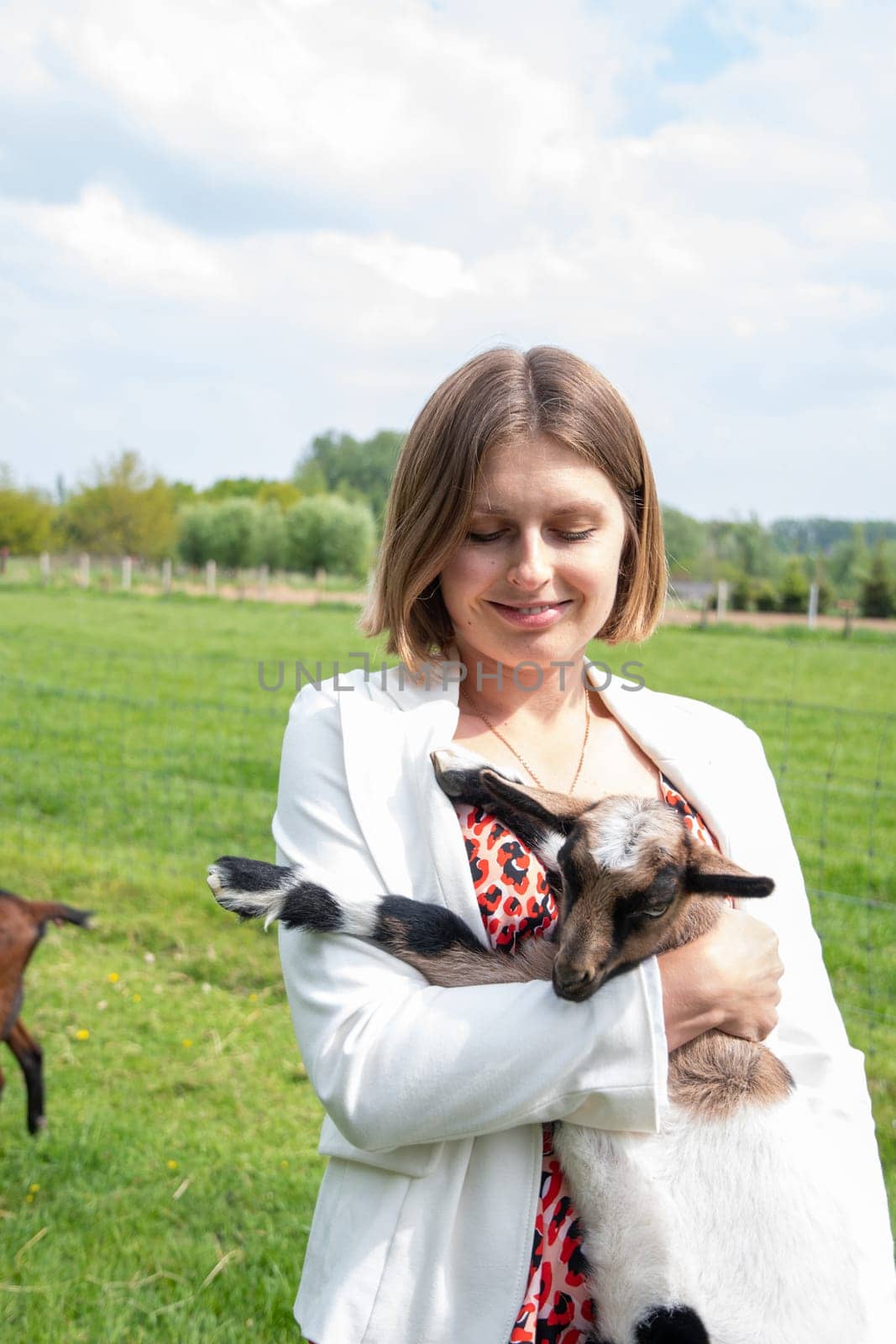 Young woman plays with goat kids, feeding them, sun shining over farm in background, High quality photo