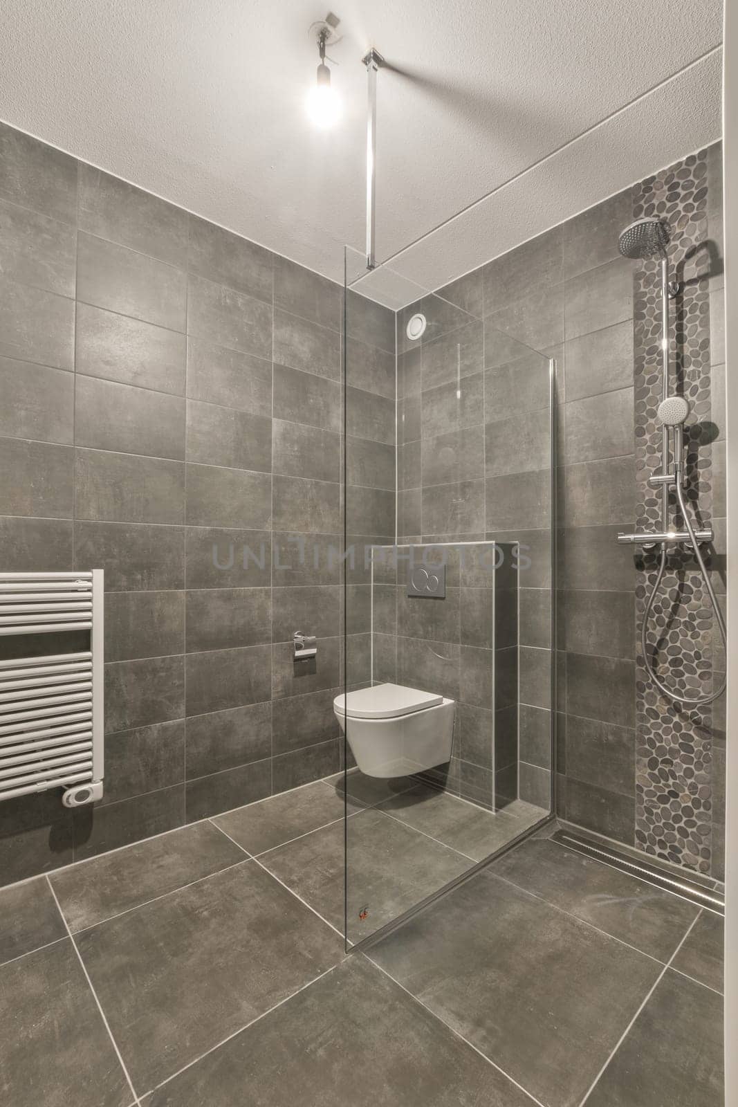 a modern bathroom with grey tiles on the walls, and a white toilet in the corner of the shower stall