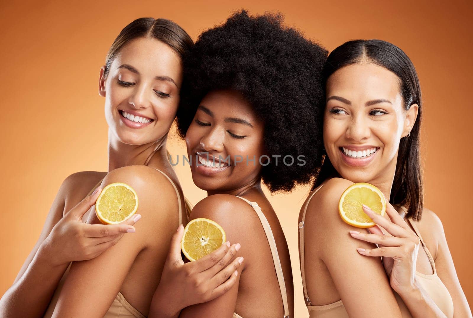Skincare, diversity and women, beauty and lemon for health, wellness and nutrition on orange studio background. Friends, smile and happy models with fruit for vitamin c, healthy or glowing skin. by YuriArcurs