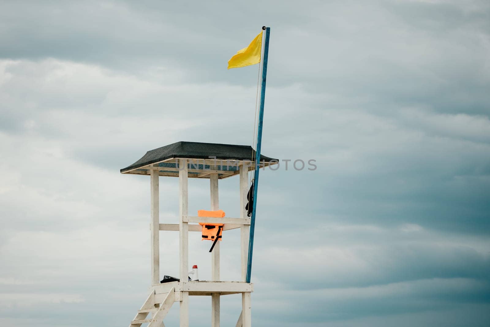 Empty white lifeguard tower with a yellow flag on the beach in windy weather. Beach lifeguard tower with yellow flag indicator. Nobody. Holiday recreation concept