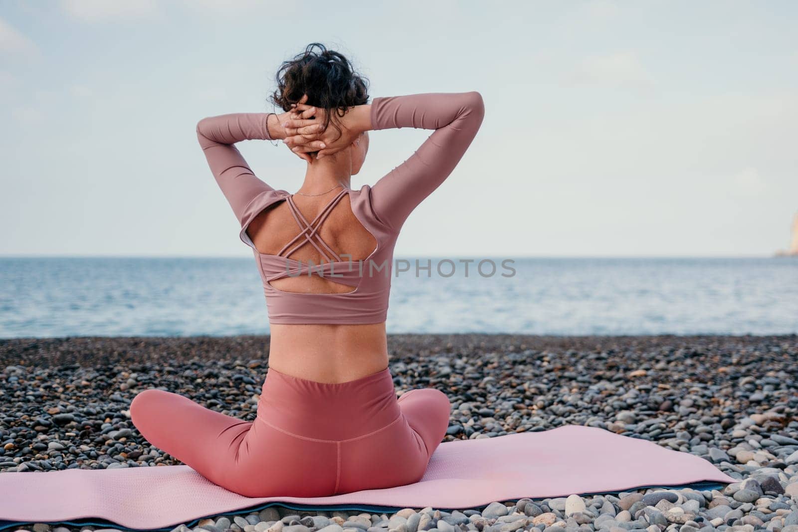 Middle aged well looking woman with black hair doing Pilates with the ring on the yoga mat near the sea on the pebble beach. Female fitness yoga concept. Healthy lifestyle, harmony and meditation.