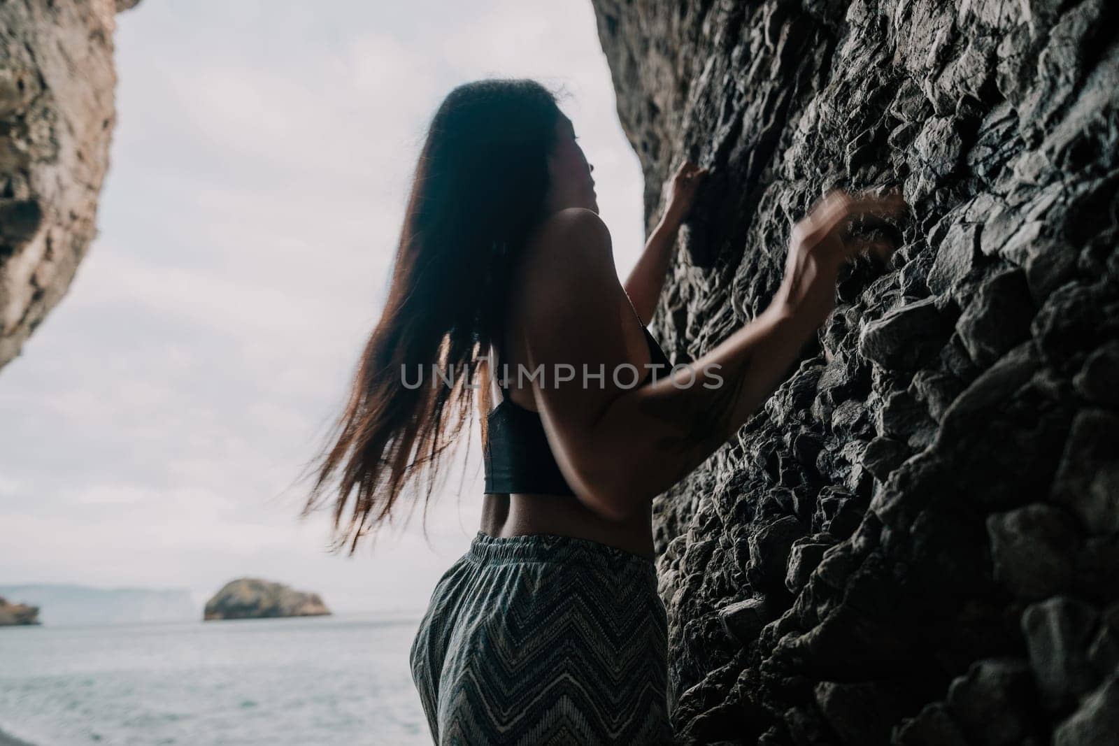 A girl climbs a rock. The athlete trains in nature. Woman overcomes difficult climbing route. Extreme hobby. Tourist woman rock climber hiking on mountains rocks over beautiful sea coast