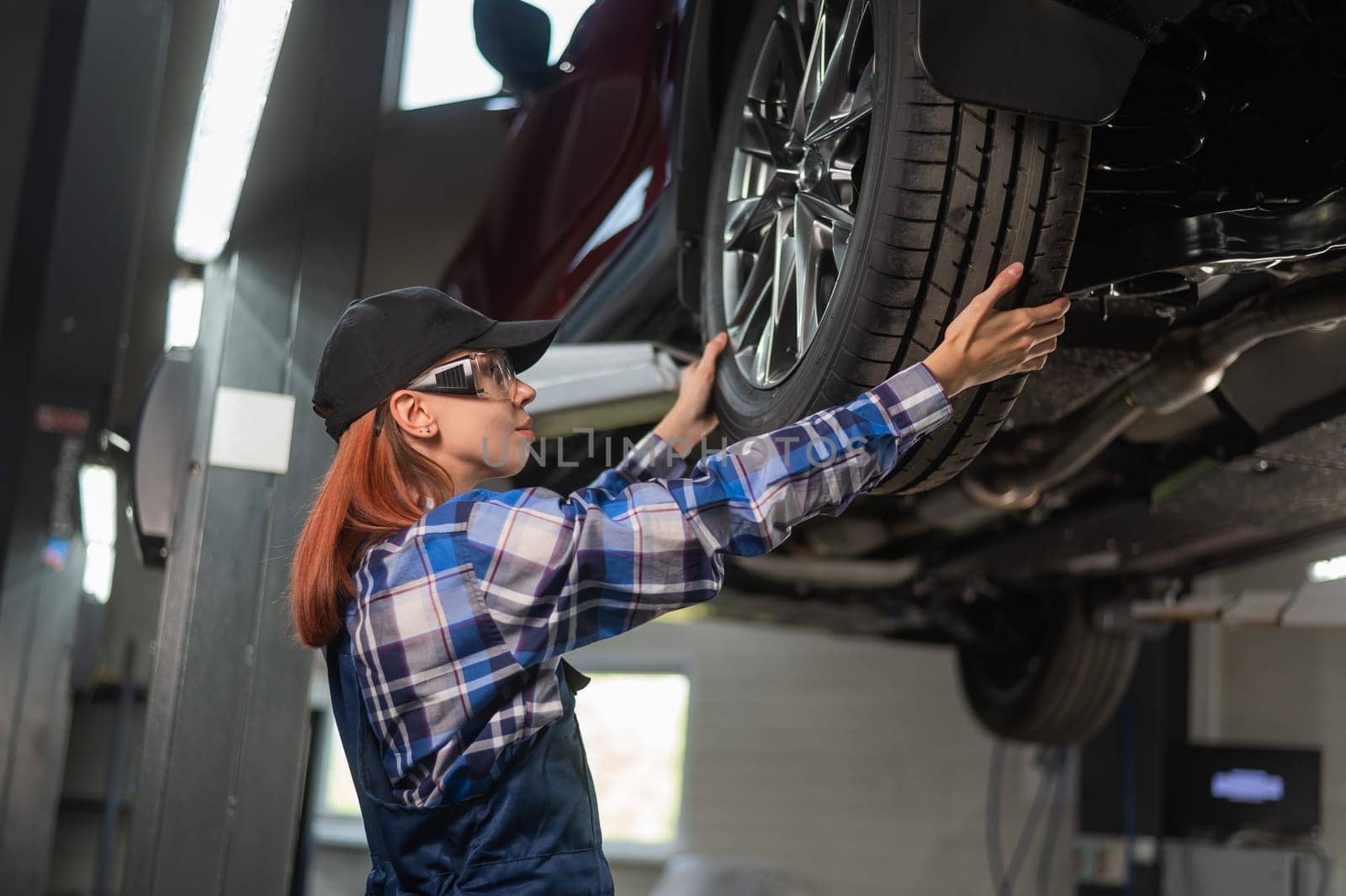 Female mechanic adjusting the tire of the car that is on the lift. A girl at a man's work