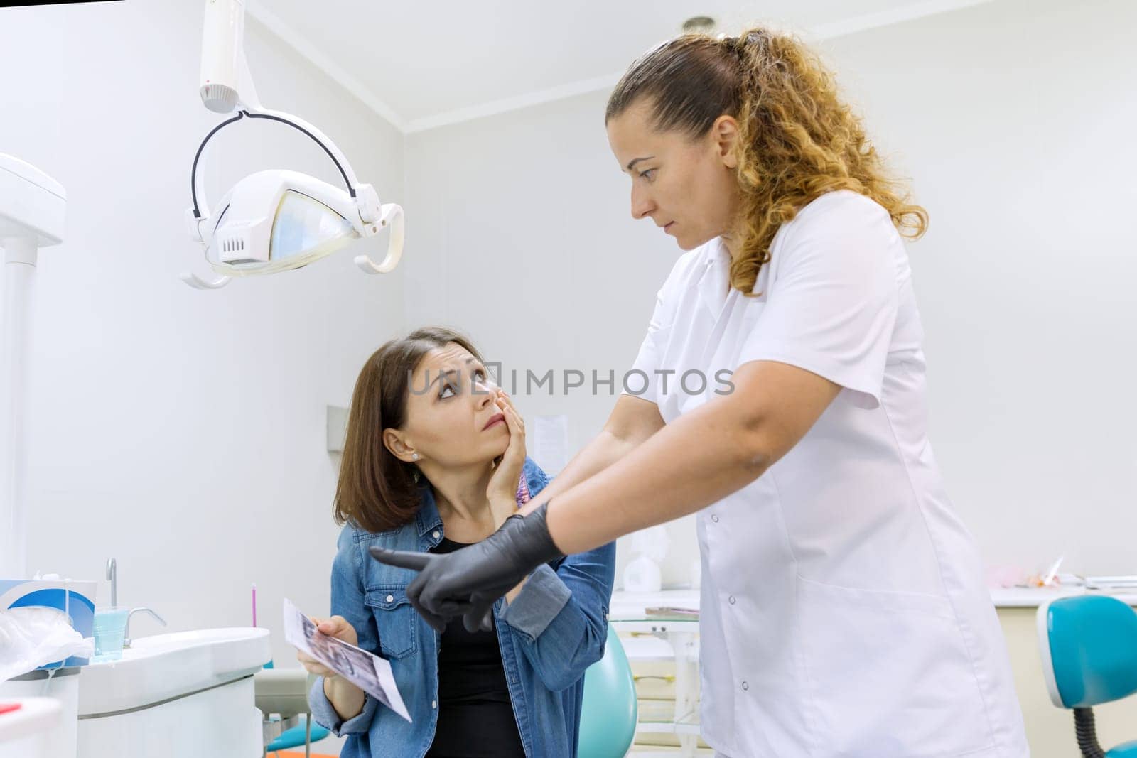 Dentist talking to woman patient in dental chair. by VH-studio