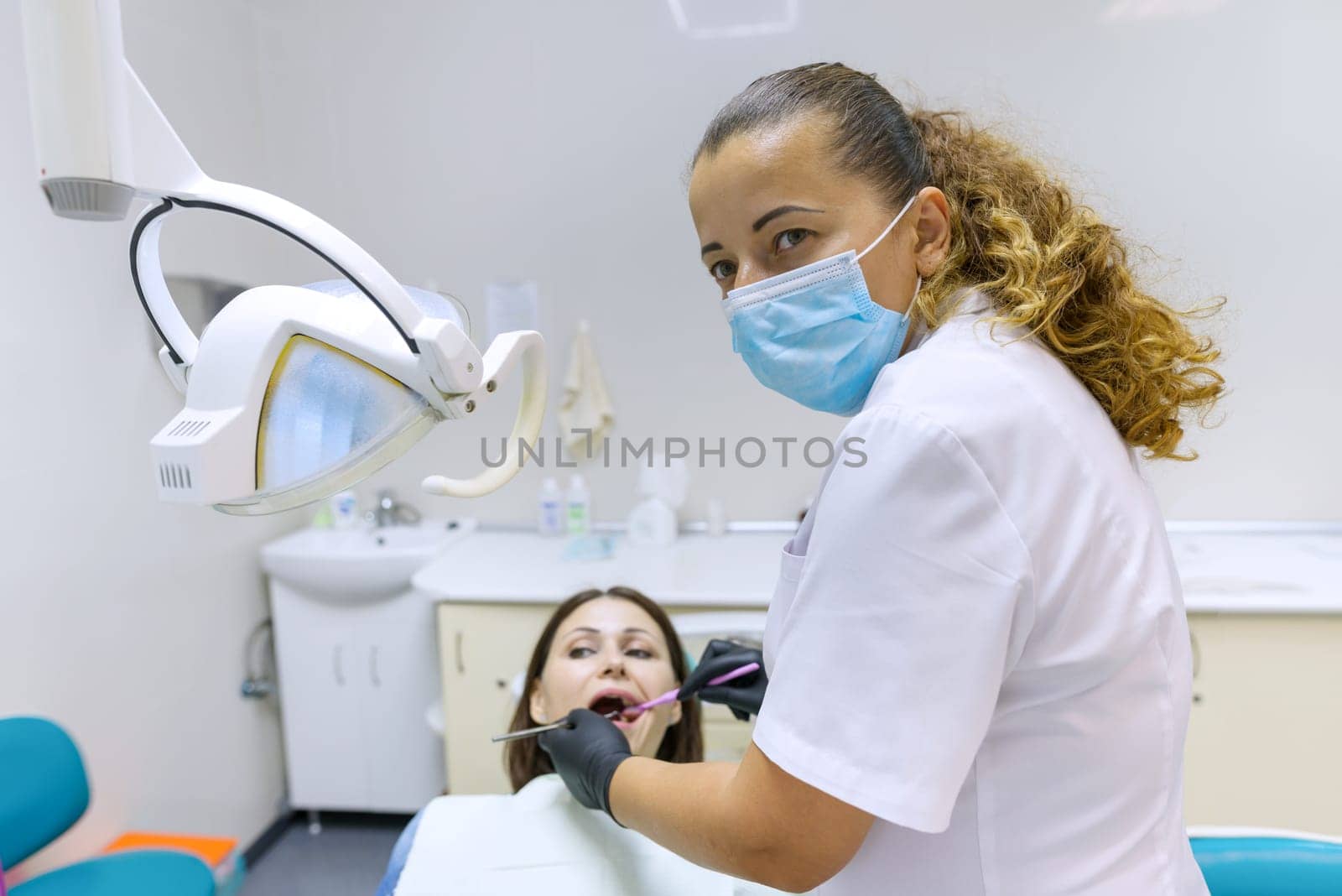 Portrait of positive mature female dentist treating patient in dental chair. Healthcare, medical and dentistry concept
