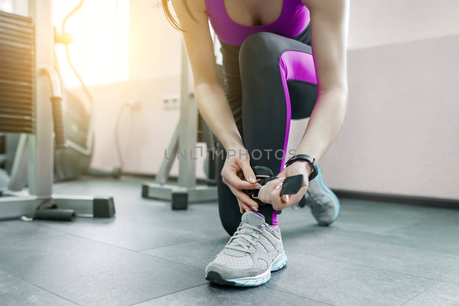 Young woman wearing leather ankle straps prepares to exercise on fitness machine in the gym. Fitness, sport, training, people concept