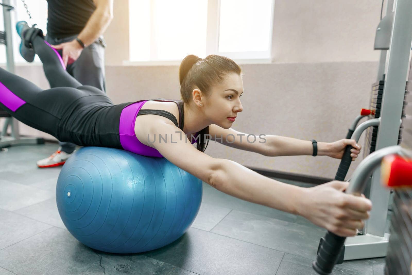 Young woman doing rehabilitation exercises with personal instructor using kinesi machine, fitness gym background. Kinesis technology, kinesitherapy, healthy lifestyle