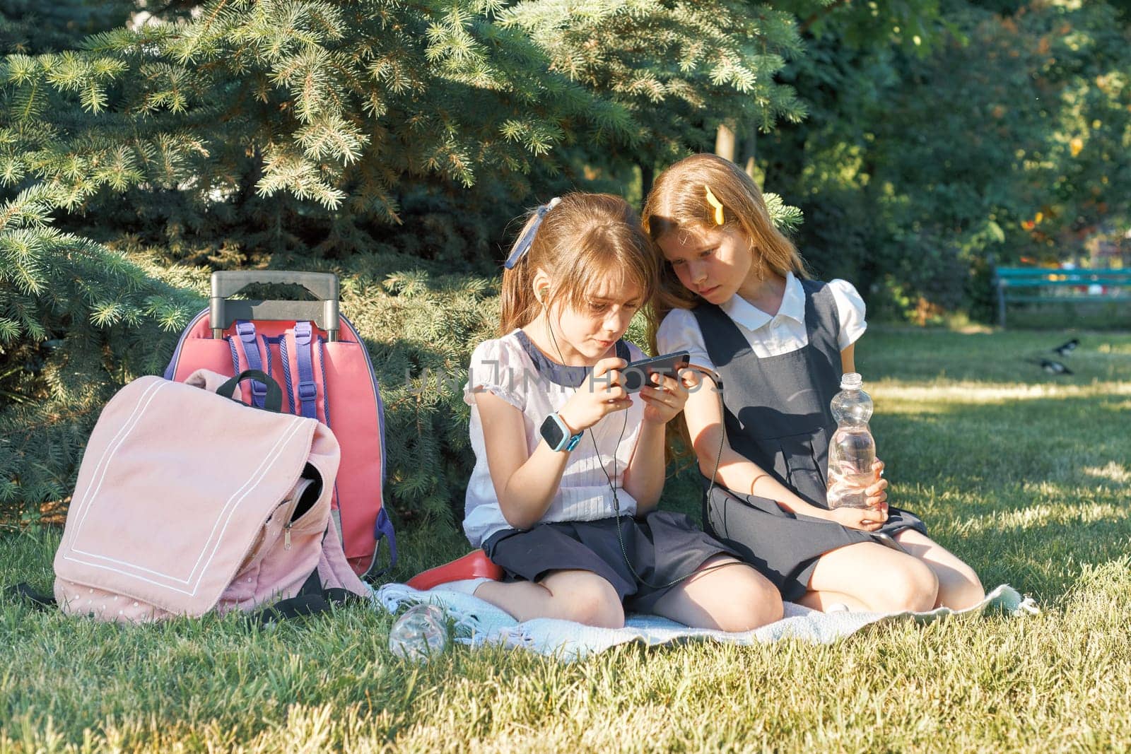 Two little schoolgirls using smartphone. Children playing, reading, looking at the phone. People, children, technology, friends and friendship concept