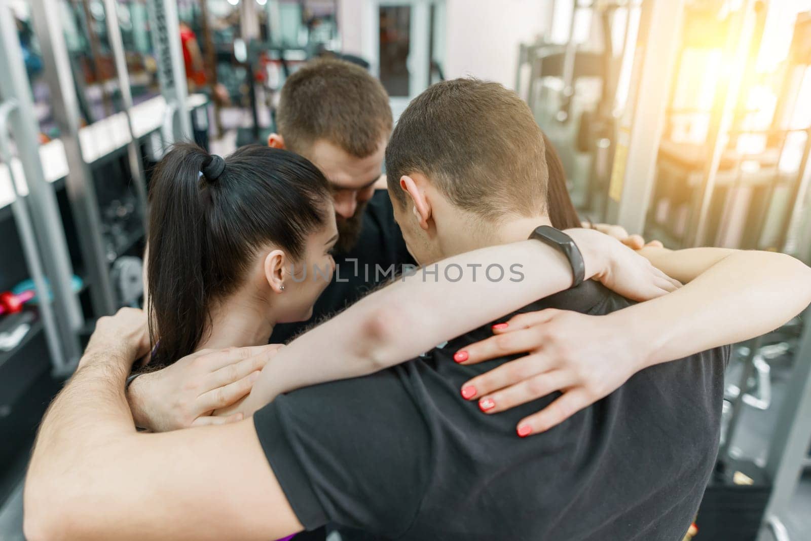 Group of young sports people embracing together in fitness gym backs. Fitness, sport, teamwork, motivation, people, healthy lifestyle concept.