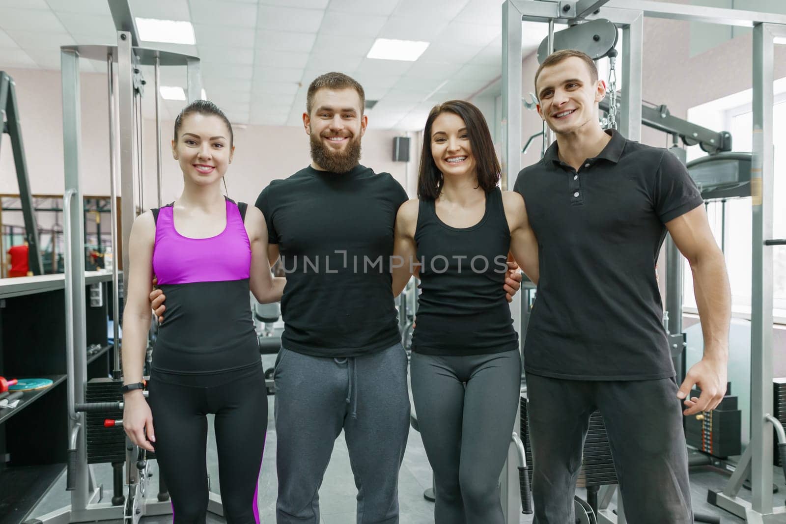 Group of young smiling sport people embracing together in fitness gym. Fitness, sport, teamwork, motivation, people, healthy lifestyle concept.