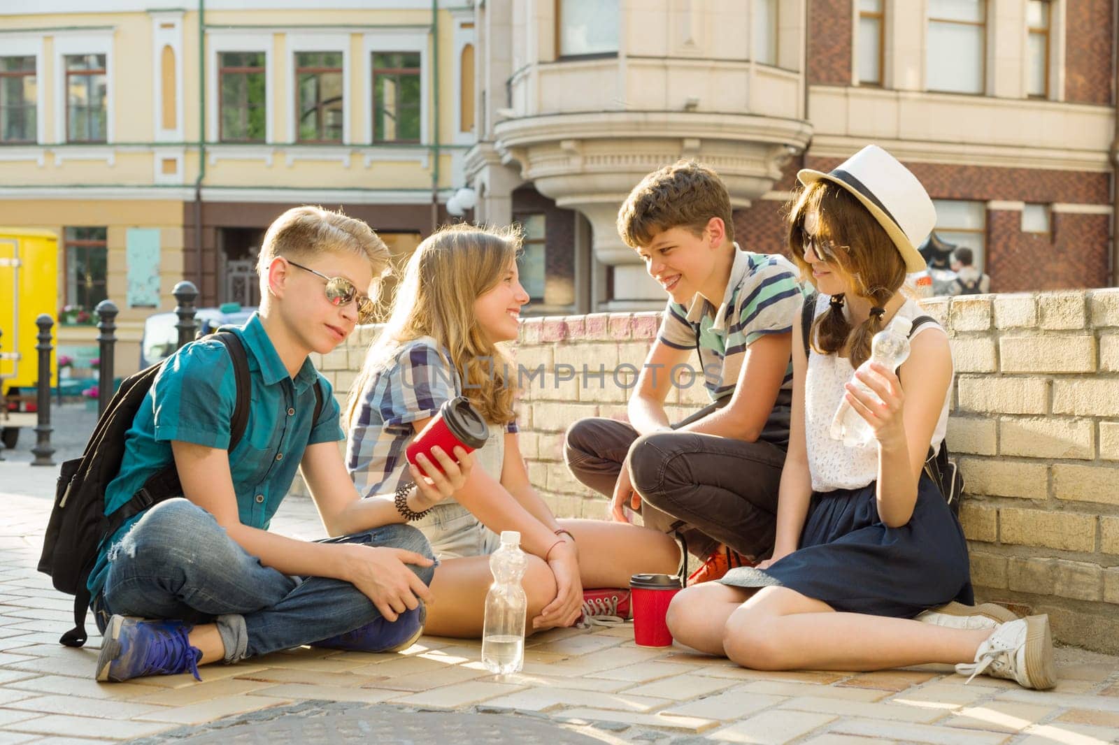 Happy 4 teenage friends or high school students are having fun, talking, reading phone, book. Friendship and people concept, city street background.