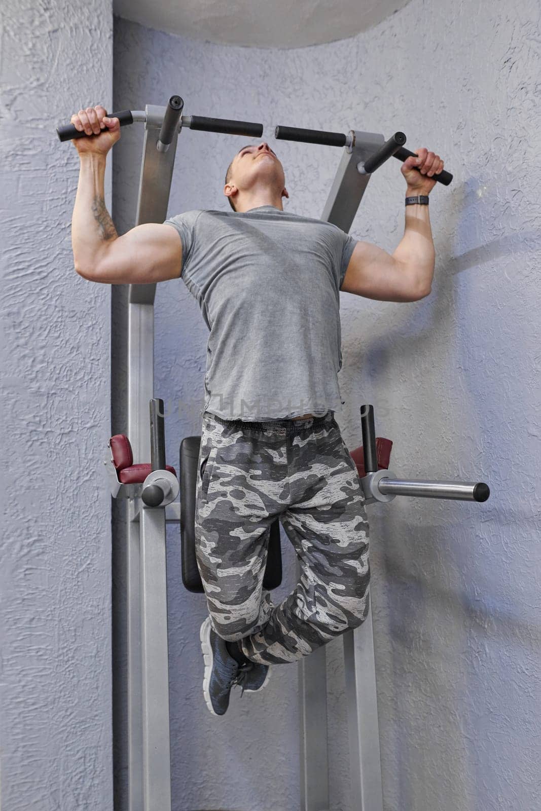Young strong muscular man in gym, male exercising, doing pull ups.