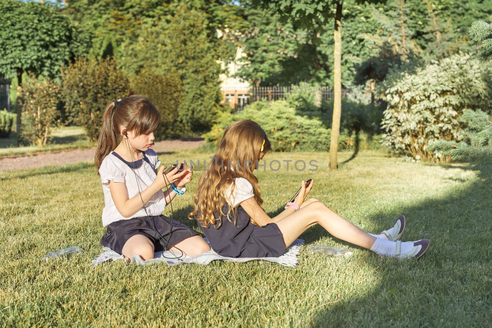 Two little schoolgirls using smartphone. Children playing, reading, looking at the phone. People, children, technology, friends and friendship concept