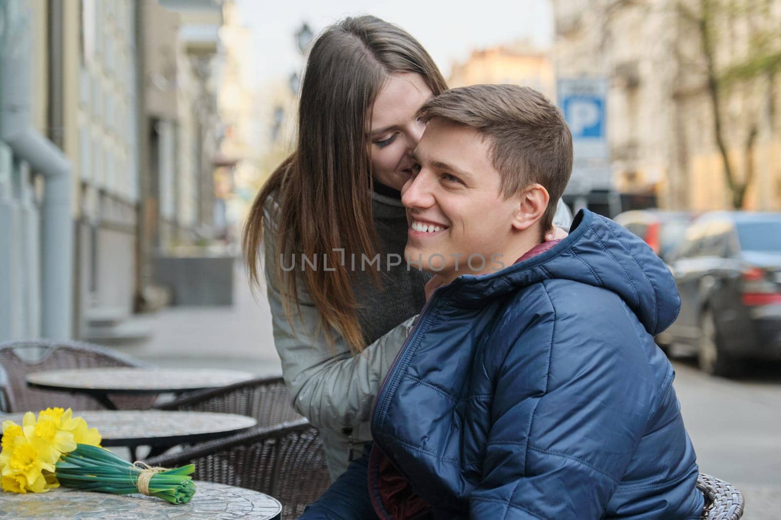 Couple in love in city. Young happy man and woman in spring city talking, walking, with bouquet of yellow flowers daffodils.