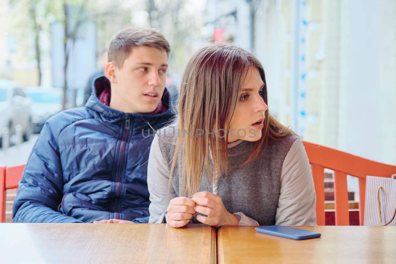 Emotional surprised young couple in outdoor cafe, sitting at the table, spring city background
