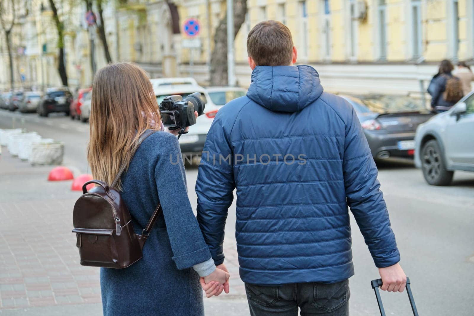 Tourists young couple walking around the city with camera suitcase, view from the back, youth traveling, winter spring season