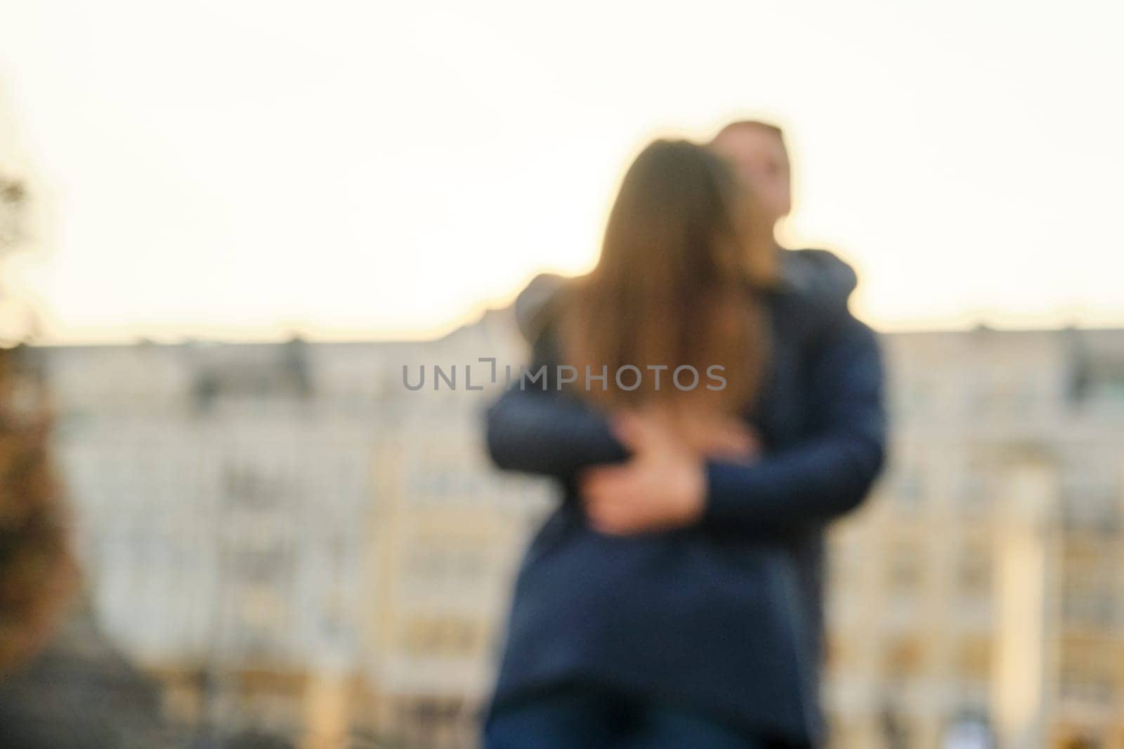 Young man and woman hugging kissing, couple blurred and soft focus, background city, golden hour by VH-studio