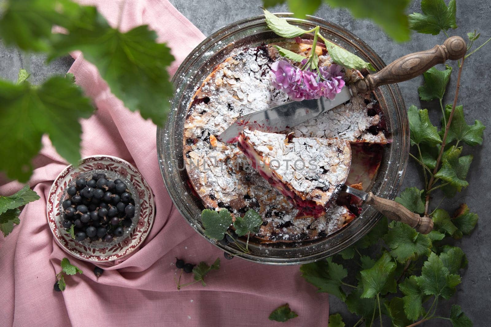 still life with delicious berry tart with almonds and black currants sprinkled with powdered sugar on a pink linen tablecloth, home bakking, top view High quality photo