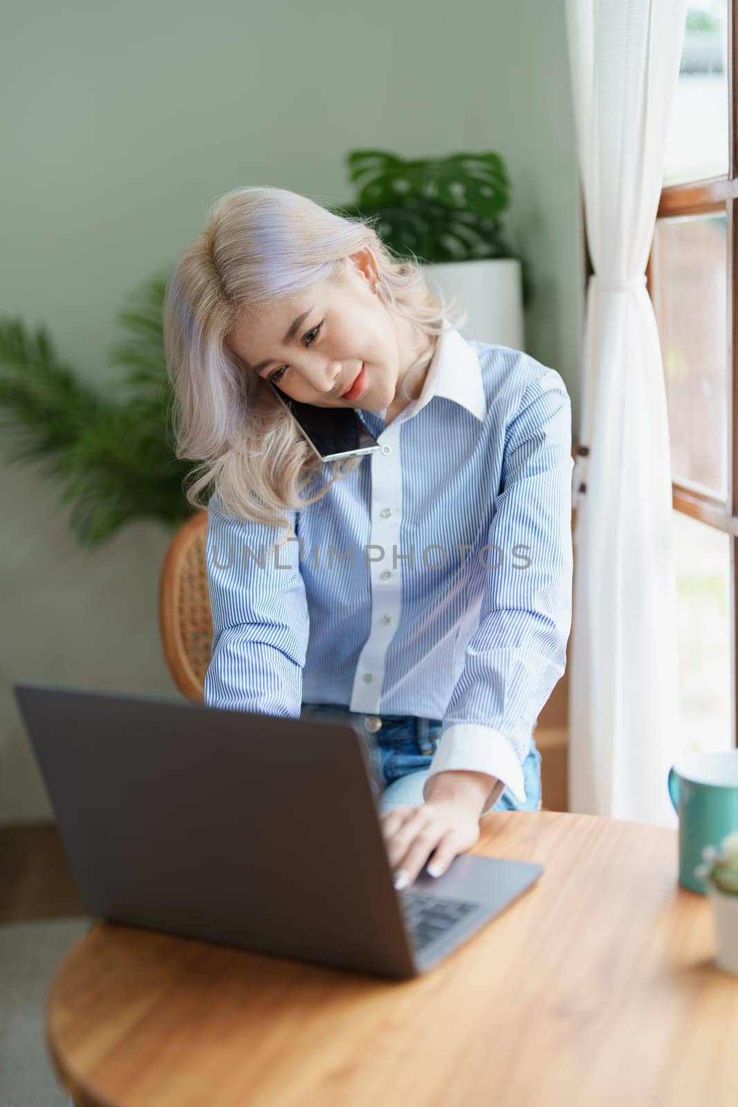 Portrait of a beautiful Asian teenage girl using her phone and computer sitting on the sofa at home.