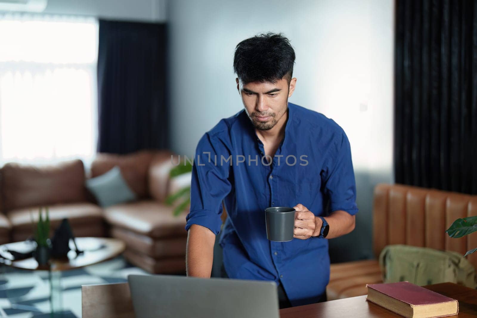 Portrait of an Asian man working on a computer and drinking coffee.