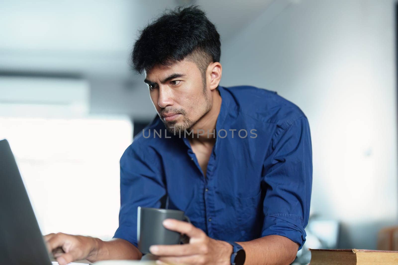 Portrait of an Asian man working on a computer and drinking coffee by Manastrong