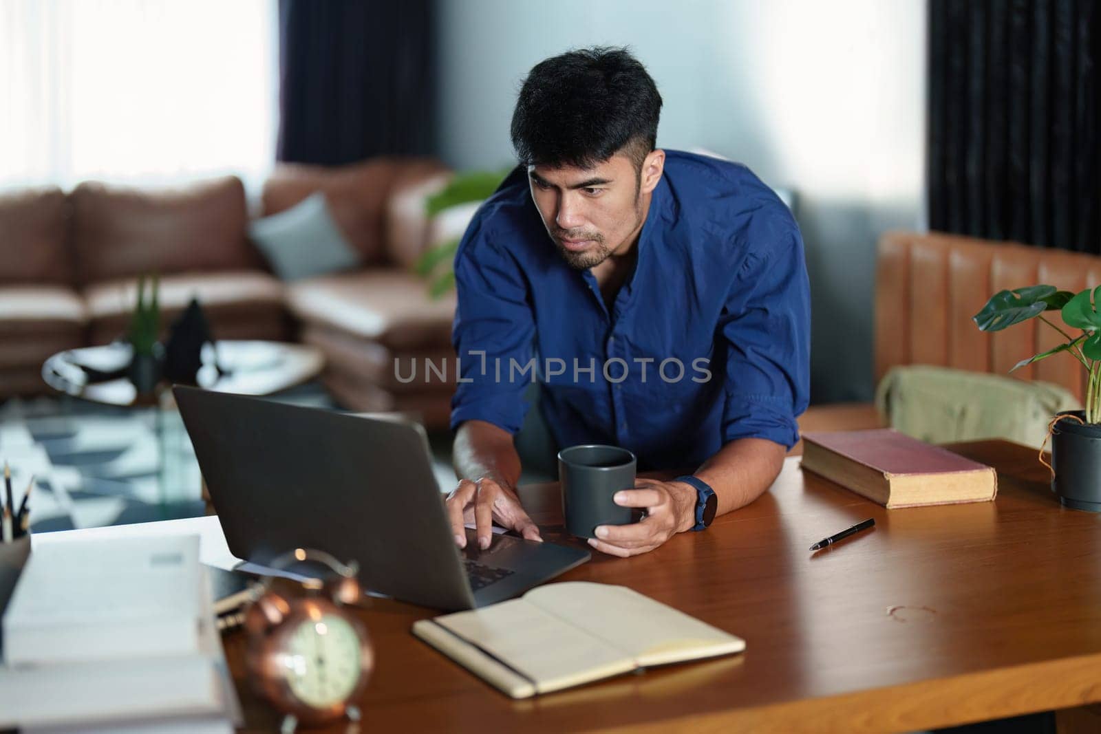 Portrait of an Asian man working on a computer and drinking coffee by Manastrong