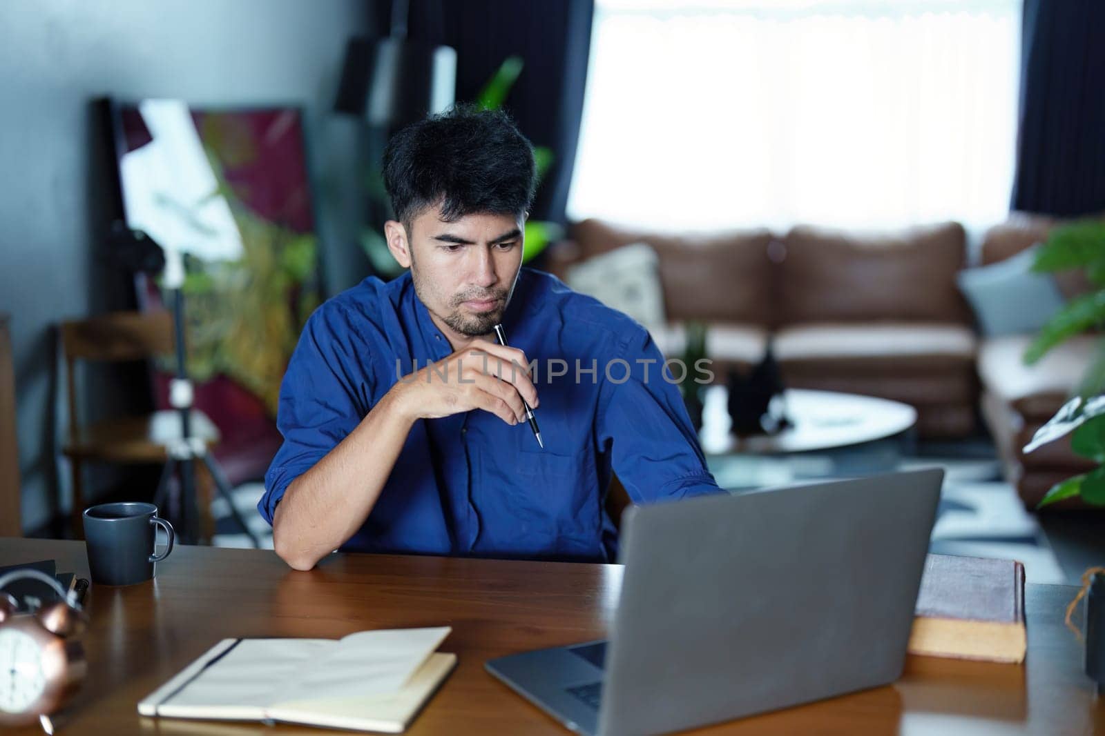 Portrait of an Asian man using a computer and note book to record his work by Manastrong