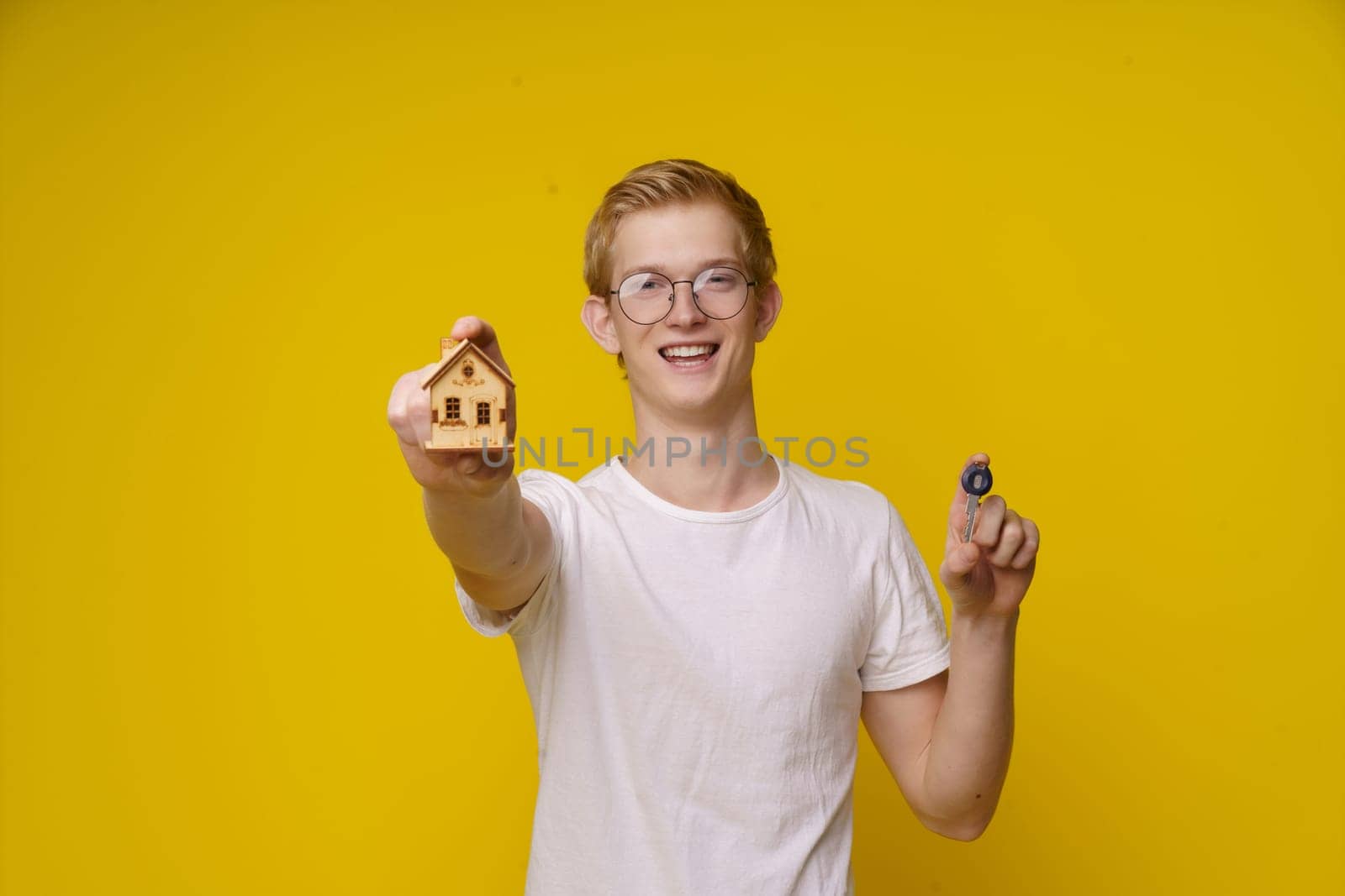 young man holds a model of a house and a key, symbolizing his independence and entry into the housing market. This image represents the concept of affordable real estate for the youth and the importance of financial planning and property ownership. by LipikStockMedia