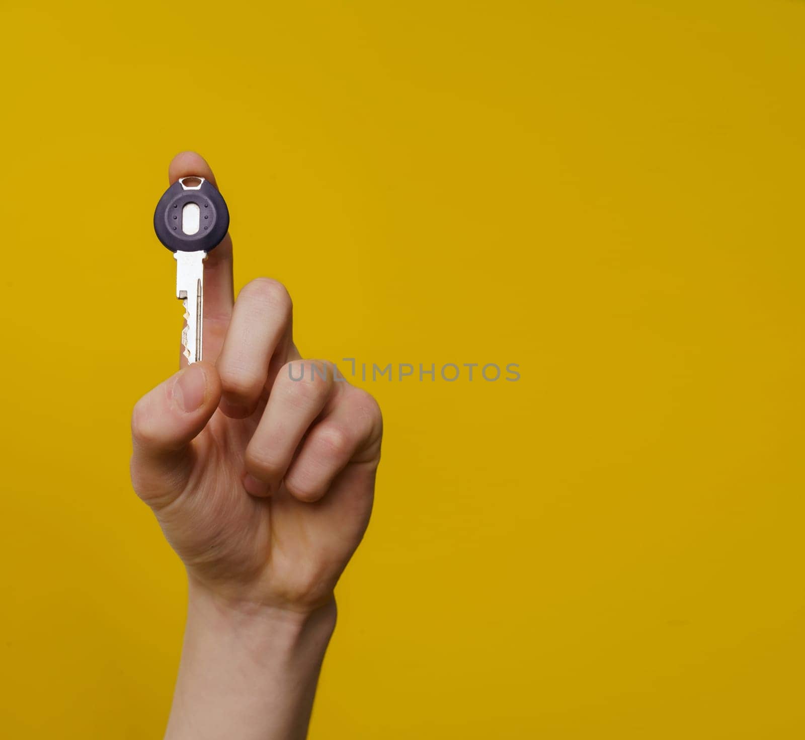 Man's hand with key isolated on yellow background with copy space. High quality photo.