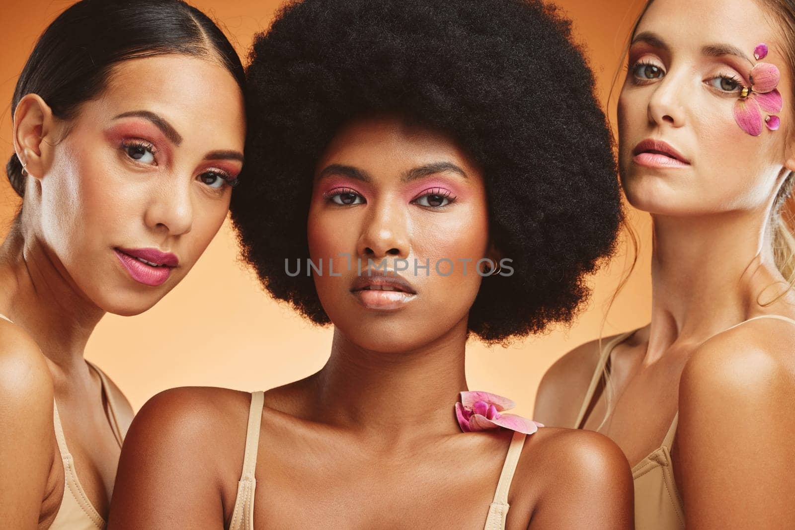 Diversity, beauty and women with flowers for makeup, skincare and cosmetics. Skincare products, spa wellness and group of girls portrait in orange studio with pink orchids for natural beauty products.