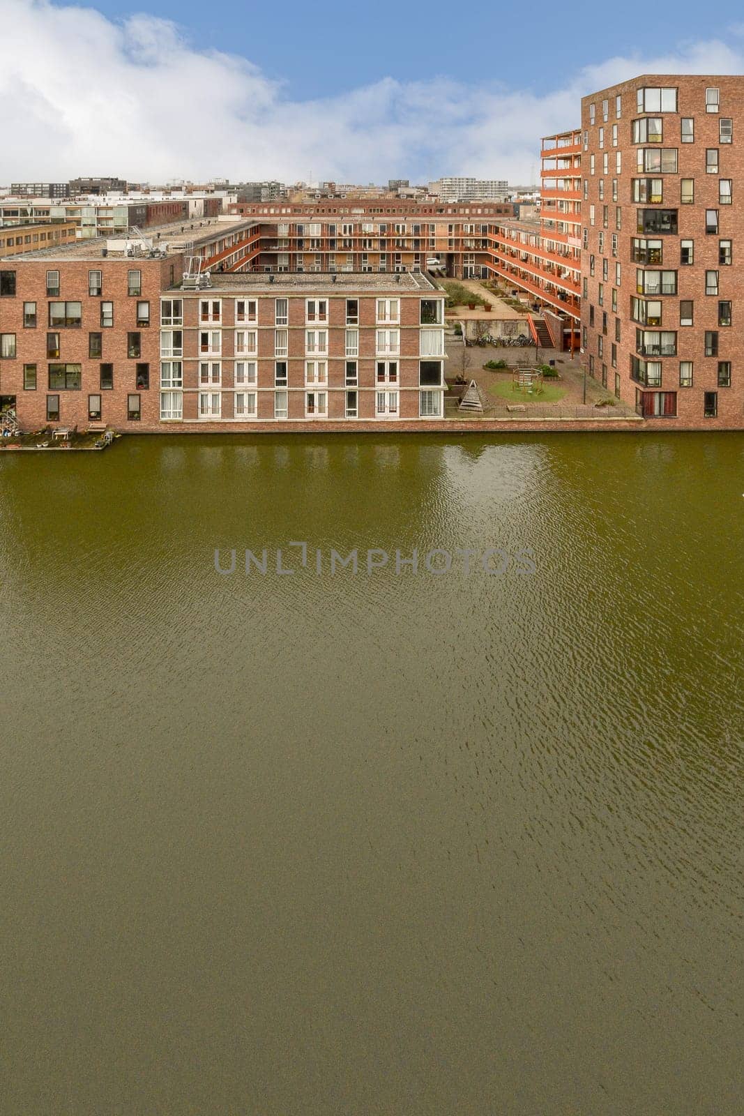 a lake with buildings in the background and blue sky above it, taken from an overpassed angle on a sunny day