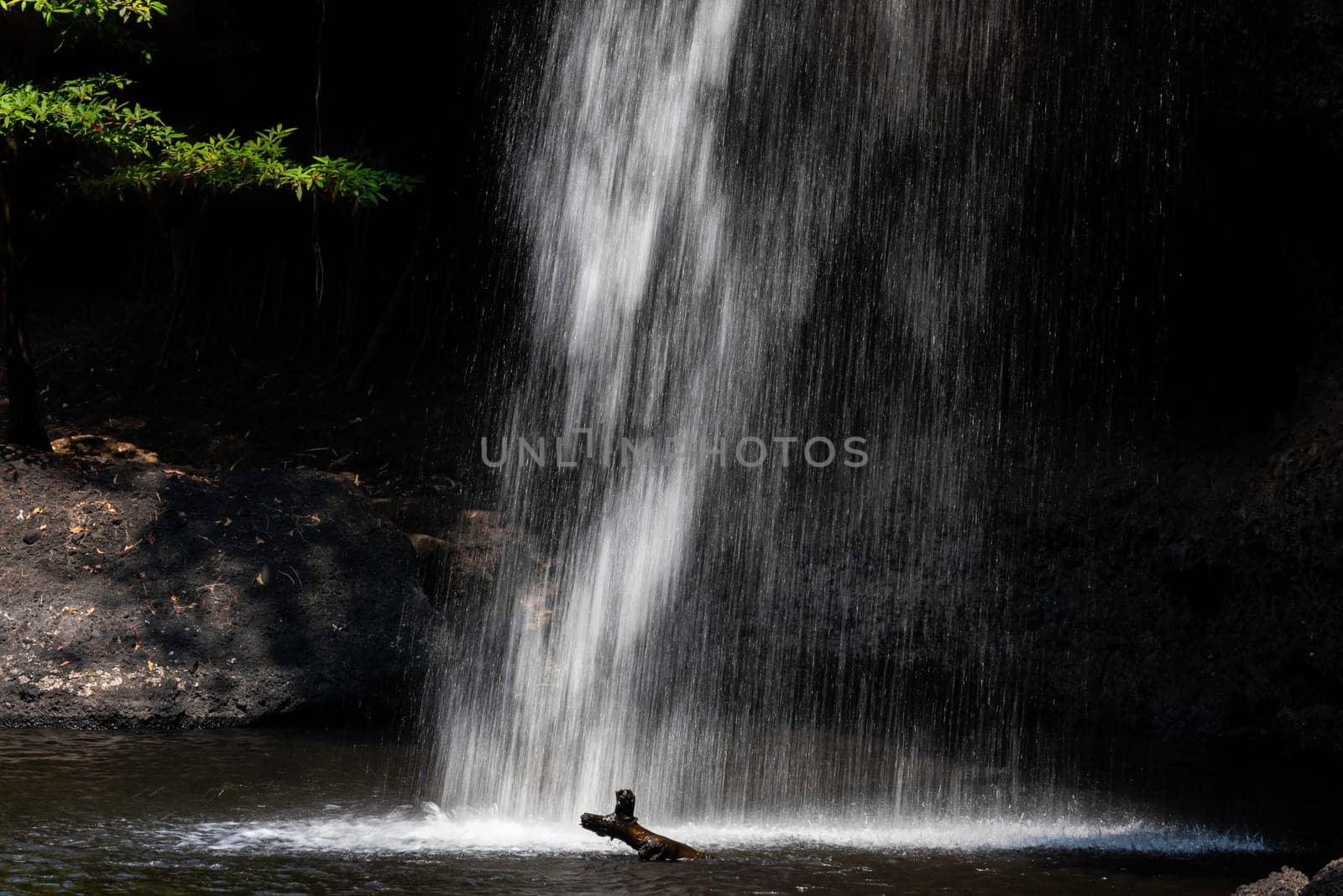 Long speed shutter technique of splashing waterfall drop on pond with dark cave inside asian tropical rainforest in summer.