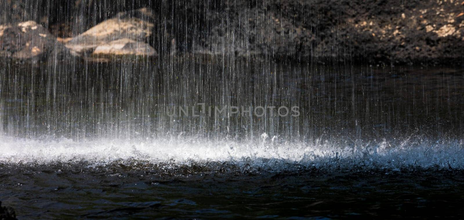 Long speed shutter technique of splashing waterfall drop on pond with dark cave inside asian tropical rainforest in summer.