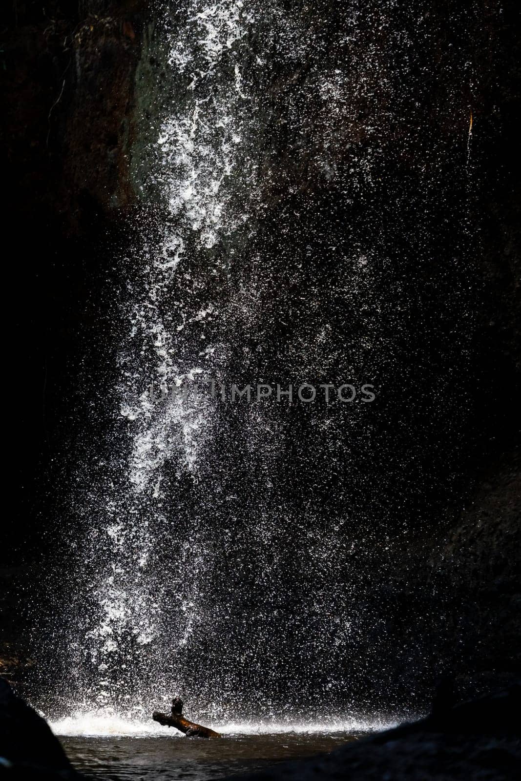 Splashing waterfall drop on pond with dark background of cave in summer.