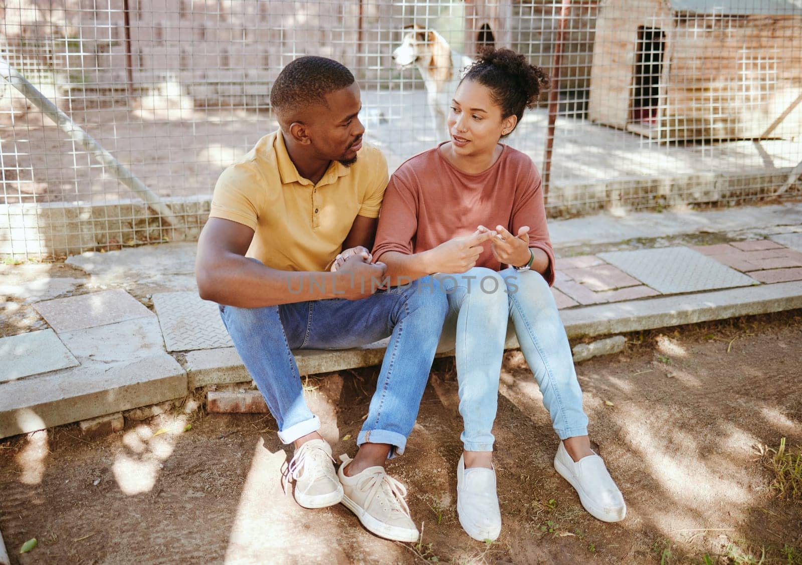 Black couple, sit and love in animal shelter, homeless canine center or foster care kennel in adoption decision choice. Talking, black woman and bonding man in pet dog charity or volunteer community.