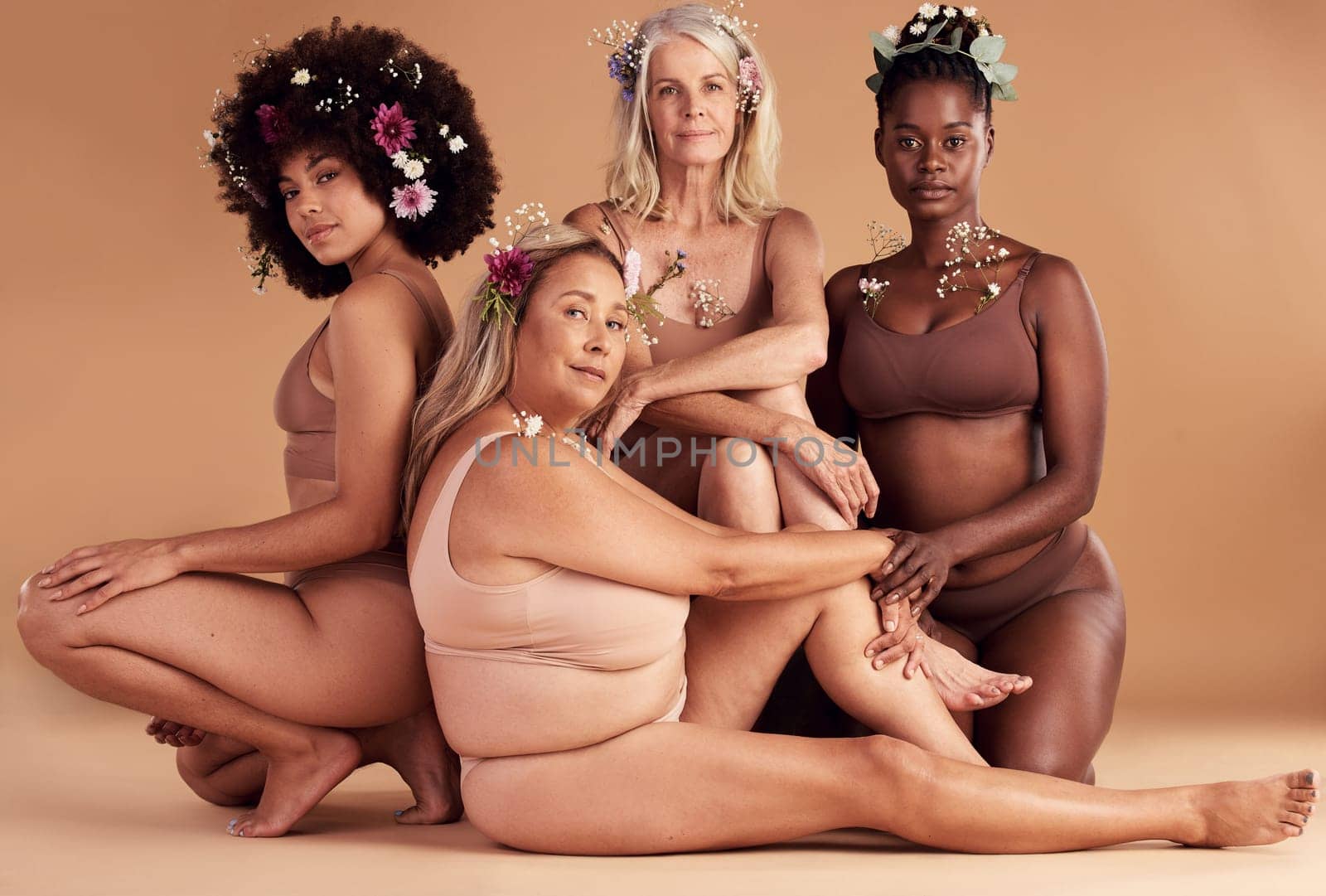 Portrait, flowers and group of women in lingerie in studio isolated on brown background. Floral cosmetics, organic makeup and body positive friends in underwear with plant product for beauty skincare.