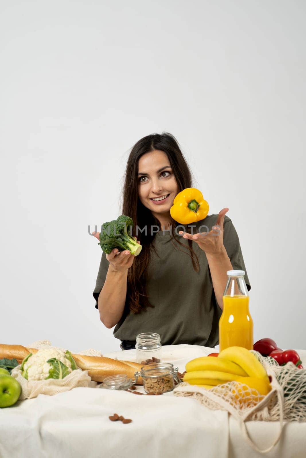 Happy woman in green t-shirt unpacking shopping mesh eco bag with healthy vegetables, fruits, bread, snacks on the kitchen at home. Healthy eating vegetarian concept