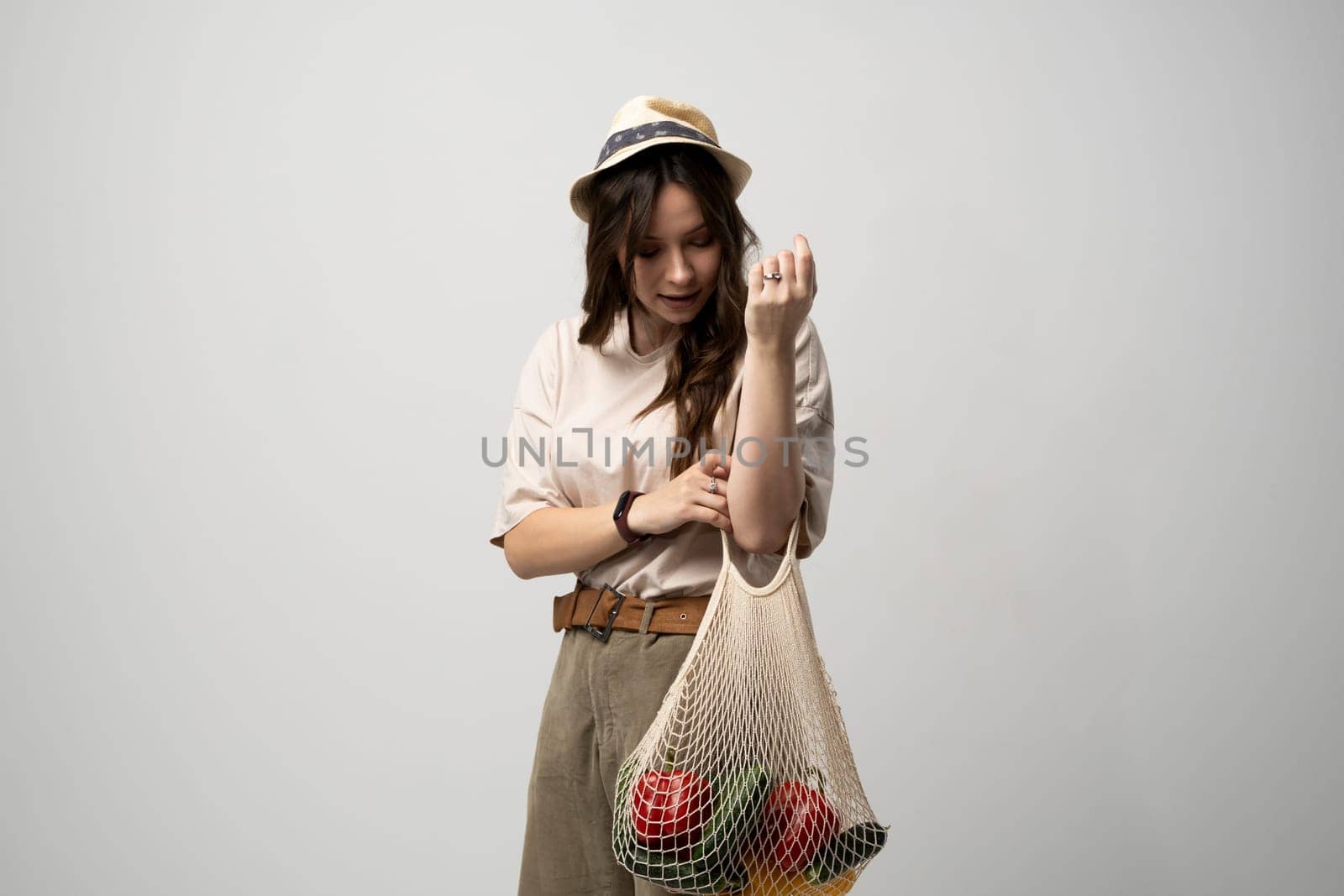 Zero waste concept. A young girl holds on her hand a textile mesh eco bag with a groceries. The girl smiles, wearing a beige t-shirt and hat. Refusal of plastic bags. by vovsht