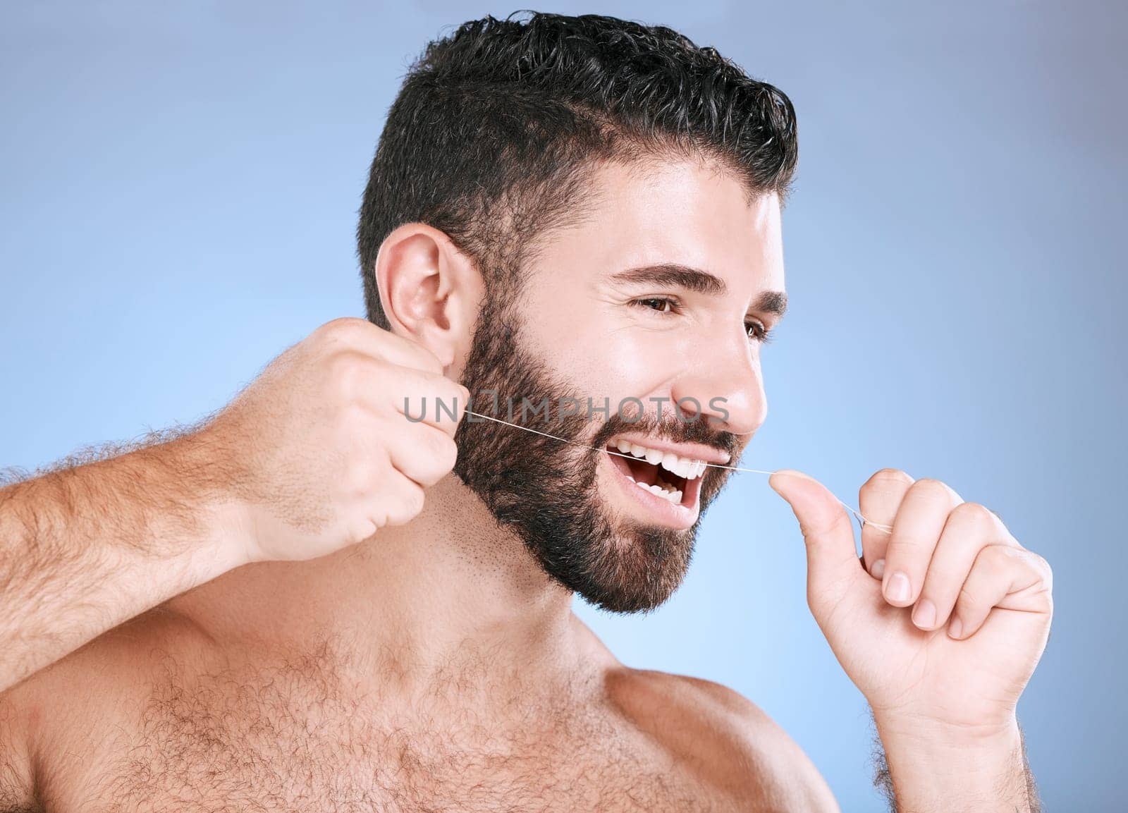Oral, floss and dental hygiene with a man in studio on a blue background cleaning his teeth for healthy gums. Dentist, healthcare and mouth with a young male flossing to remove plaque or gingivitis.
