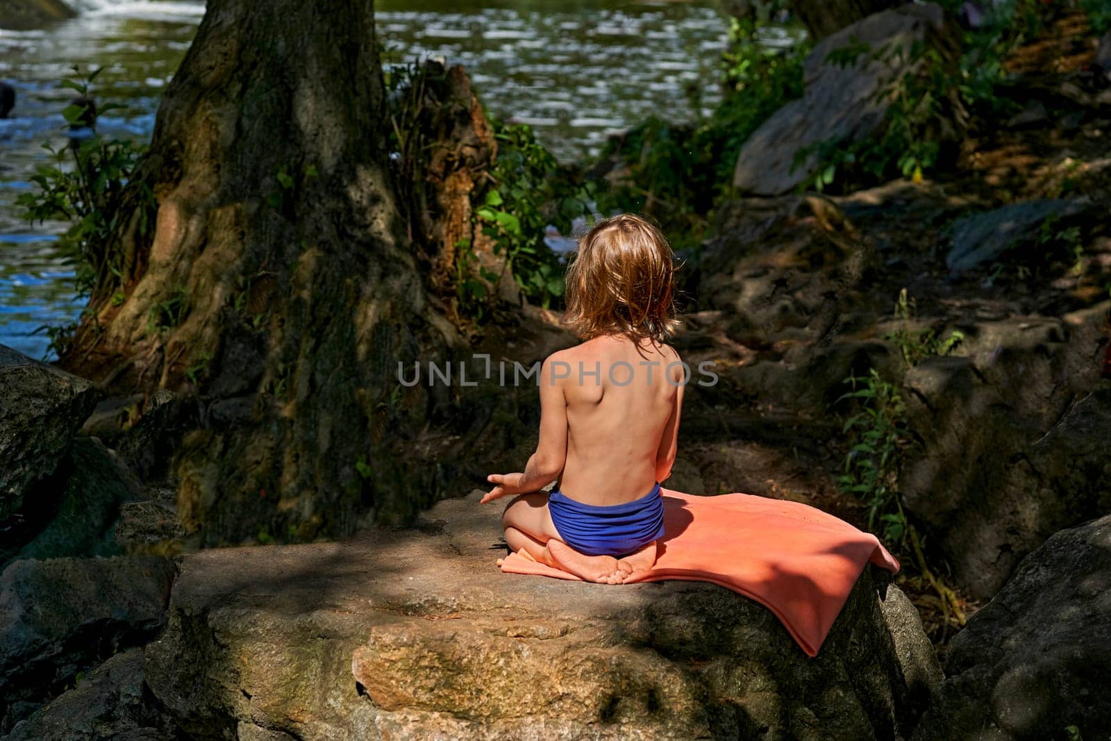 Cute child meditates resting sunbathing among the stones near the river by jovani68