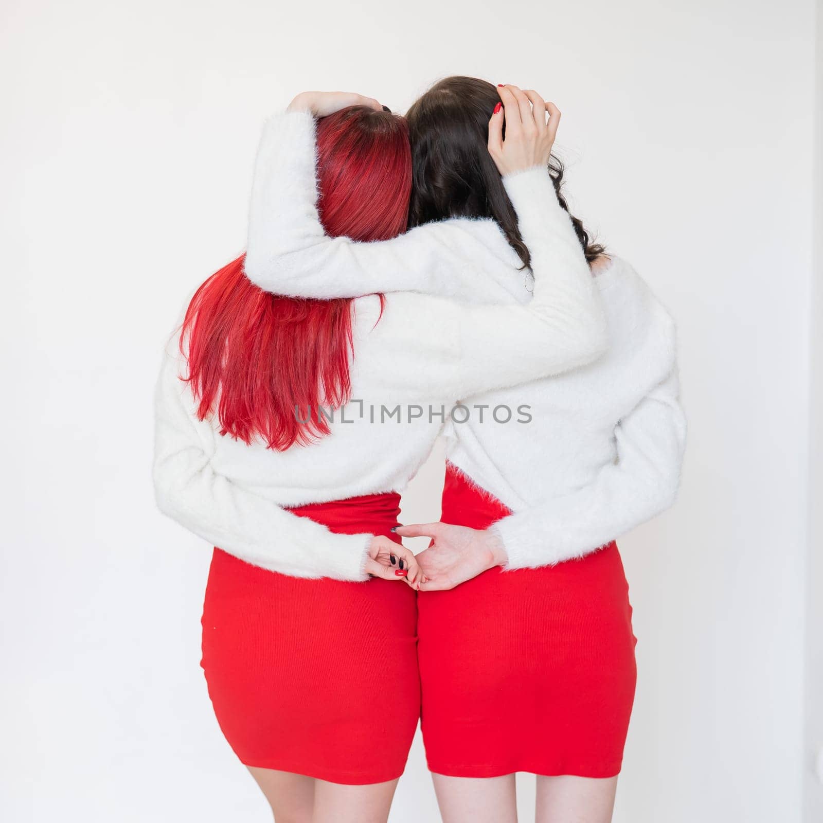 Rear view of two women dressed in identical red dresses and white sweaters. Lesbian intimacy. White background. by mrwed54
